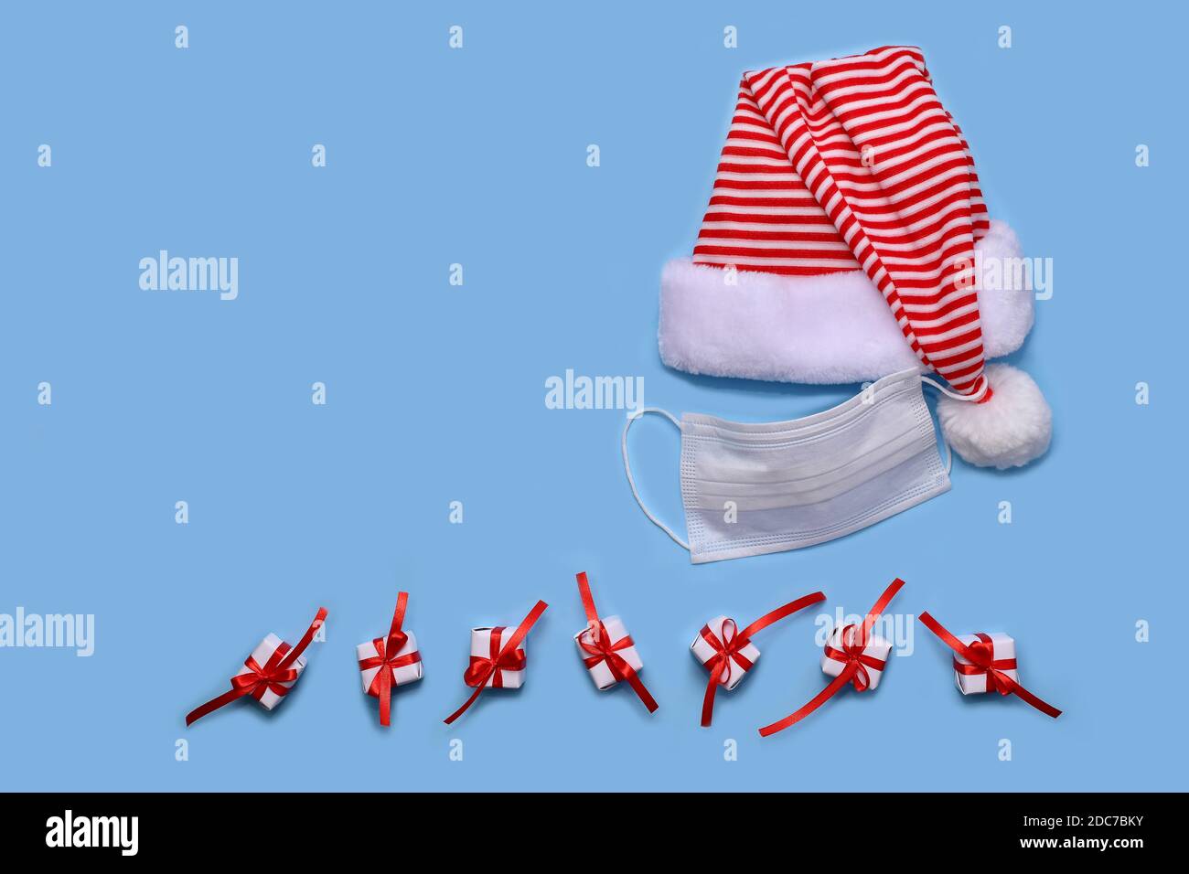 Chapeau de père Noël rayé, avec un masque de protection suspendu sur le pompon. Aux boîtes cadeaux, attaché avec un ruban avec un noeud. Banque D'Images