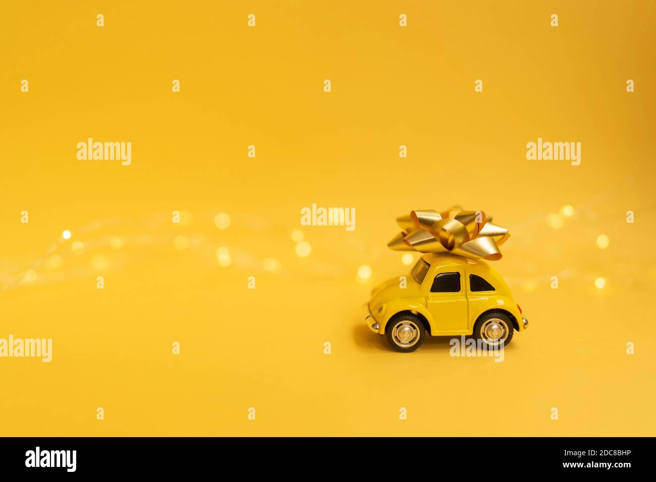 Une voiture jaune avec un noeud doré sur son dessus avec des lumières bokeh sur fond jaune Banque D'Images