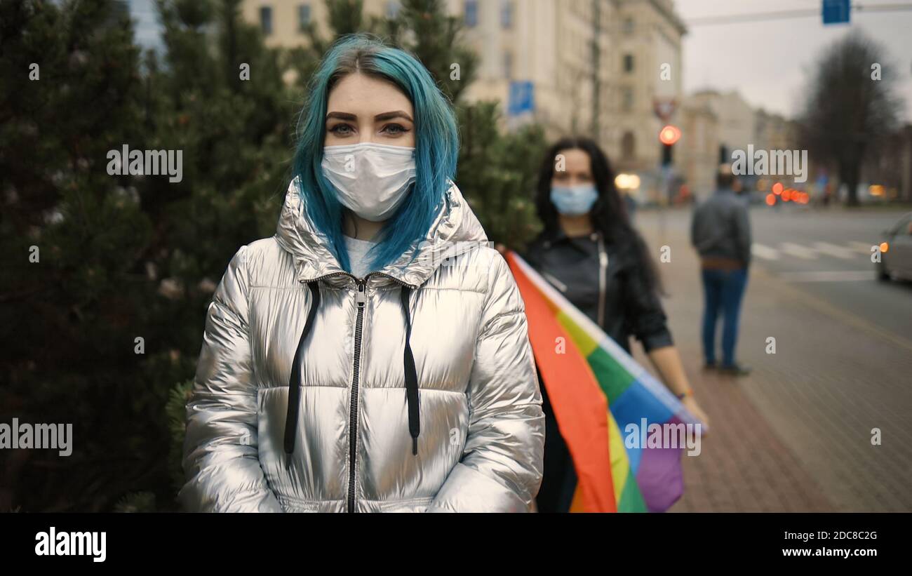 Deux femmes lesbiennes dans des masques médicaux avec le drapeau arc-en-ciel Banque D'Images
