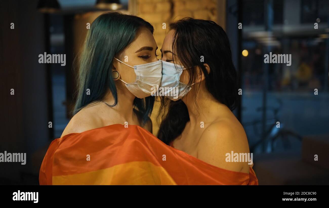 Deux femmes lesbiennes nues dans des masques médicaux avec un drapeau arc-en-ciel Banque D'Images