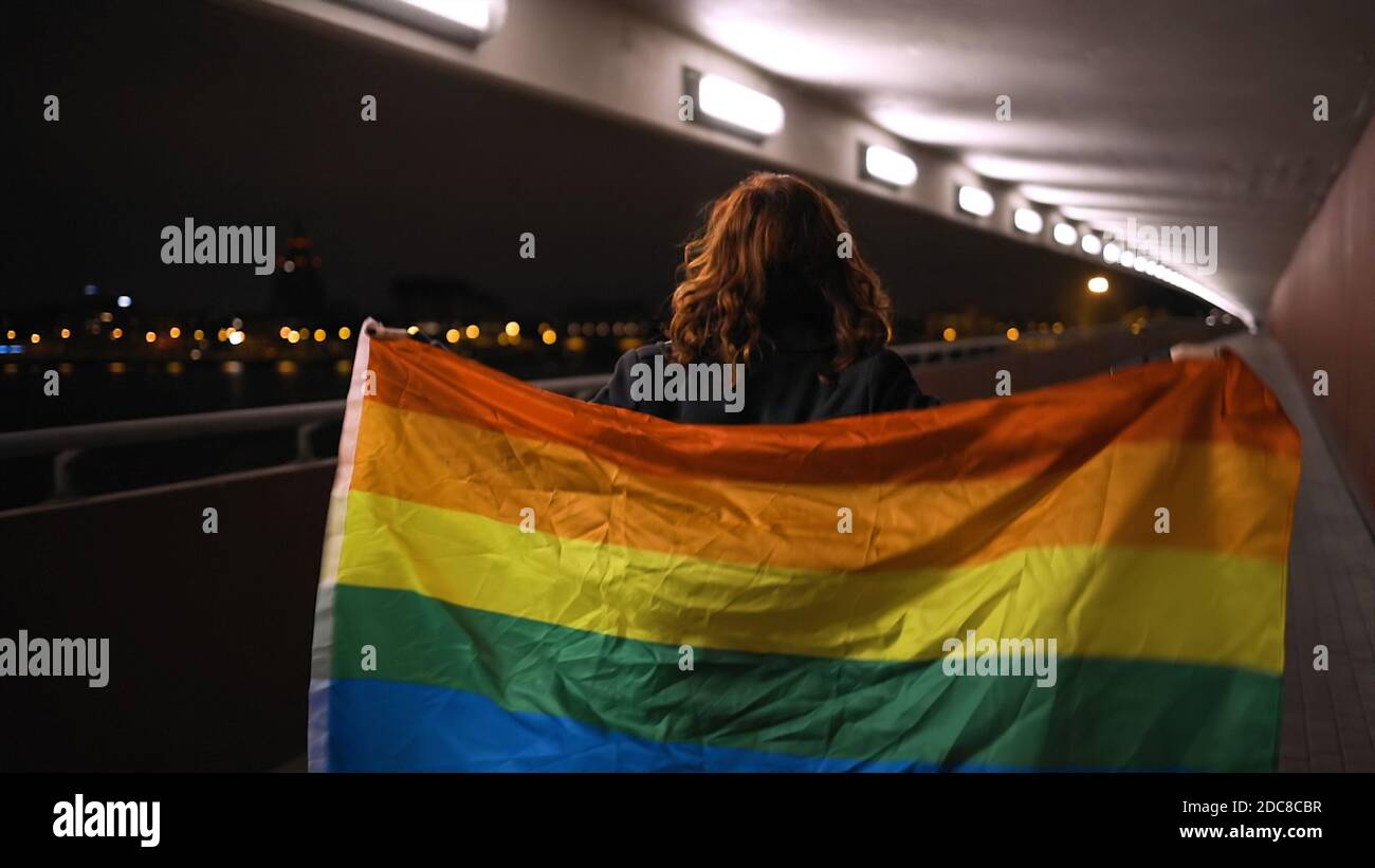 Vue arrière: Femme LGBT marchant avec un grand drapeau arc-en-ciel Banque D'Images