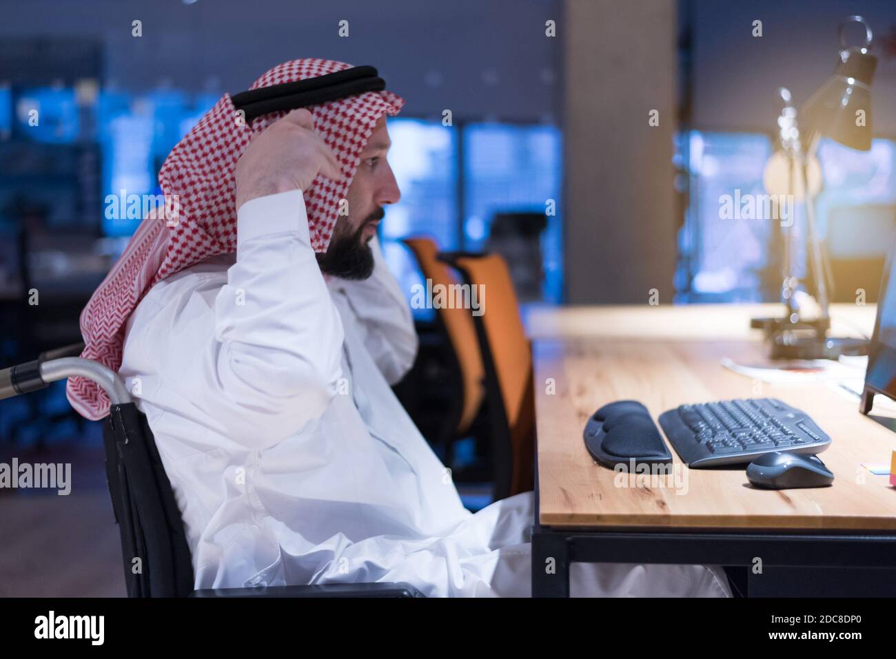 Homme d'affaires arabe handicapé dans la tradition suit travaillant en fonction pendant la pandémie de coronavirus. Homme d'affaires handicapé dans le fauteuil roulant travaille en ligne i Banque D'Images