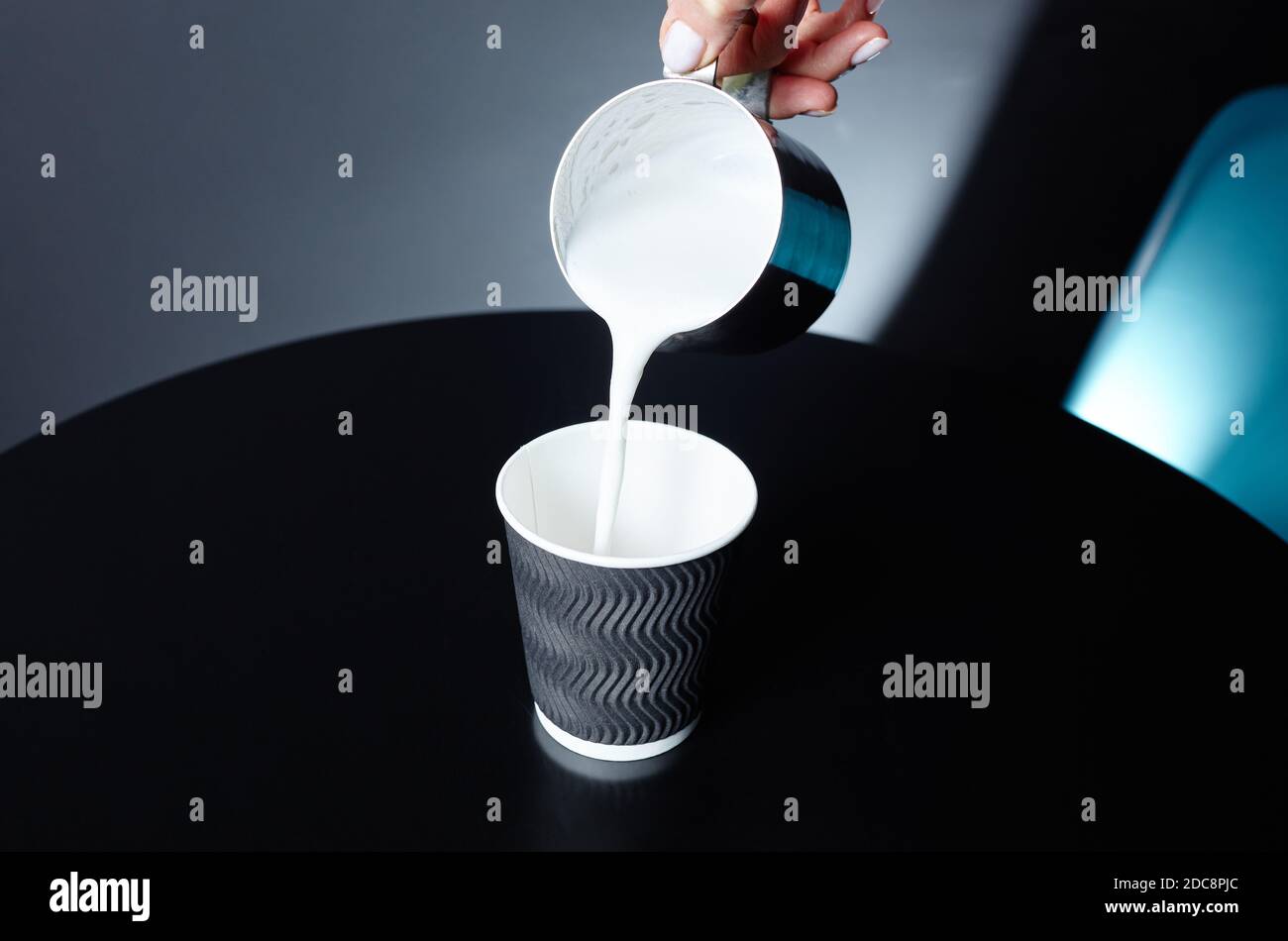 Le barista verse du lait dans une tasse en papier jetable sur une table en bois dans un café. Préparer une boisson savoureuse au lait. Une femme tient le pichet de lait en métal à la main Banque D'Images