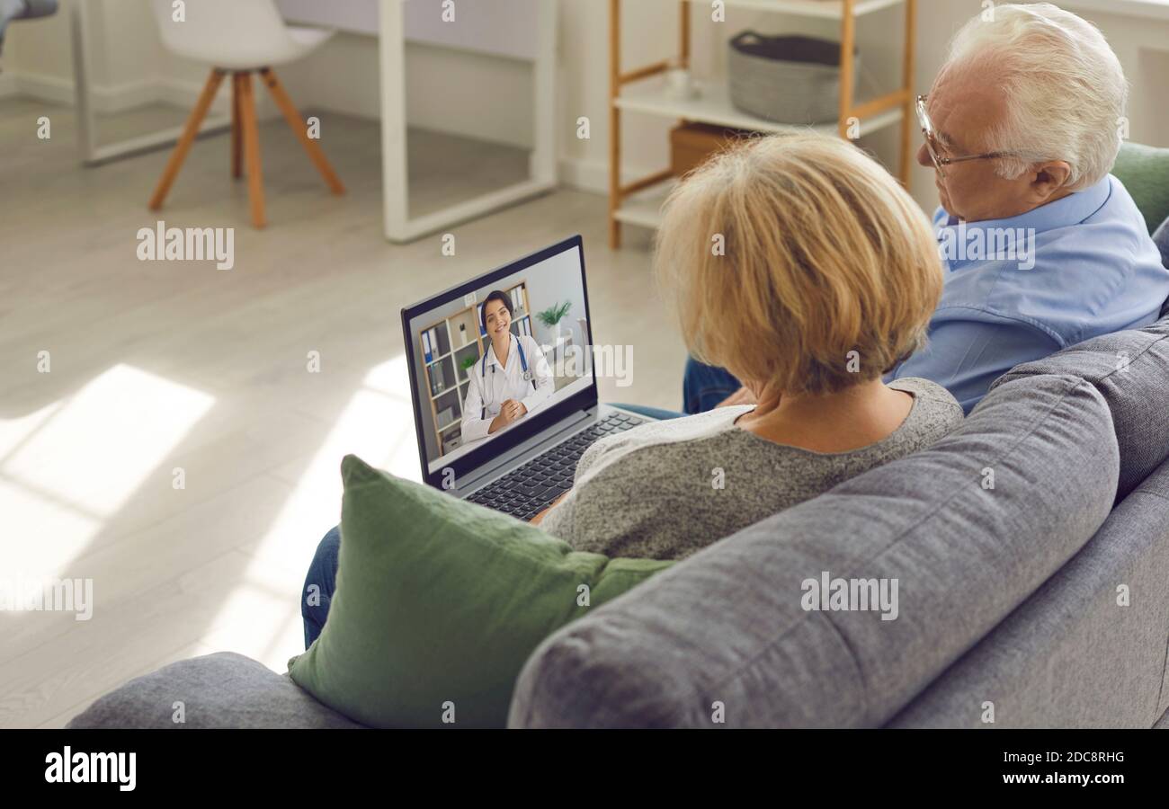 Couple senior assis sur un canapé avec un ordinateur portable et ayant la vidéo appelez un médecin en ligne Banque D'Images