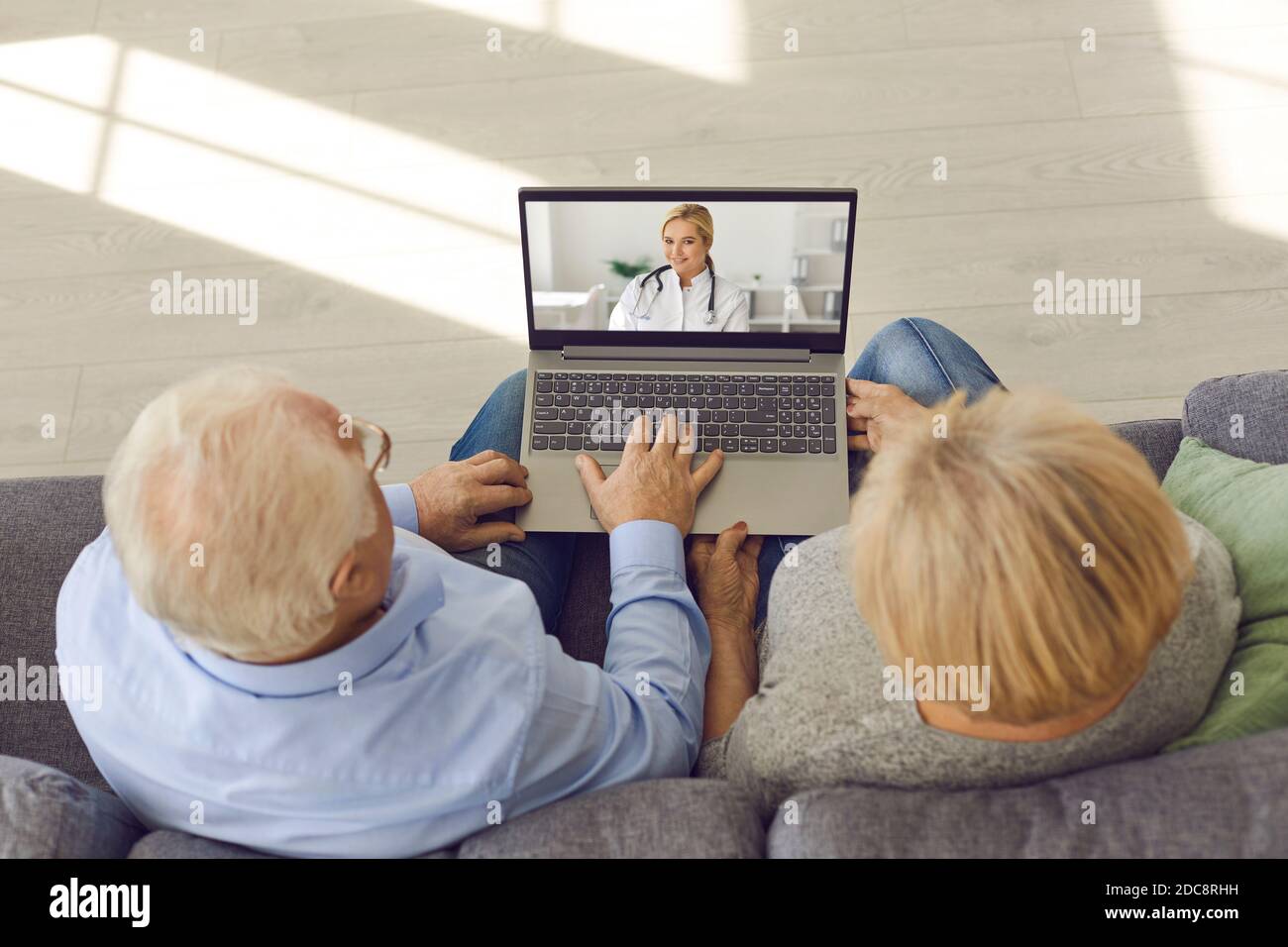 Couple senior assis sur un canapé avec un ordinateur portable et ayant un médecin consultation avec un médecin en ligne Banque D'Images