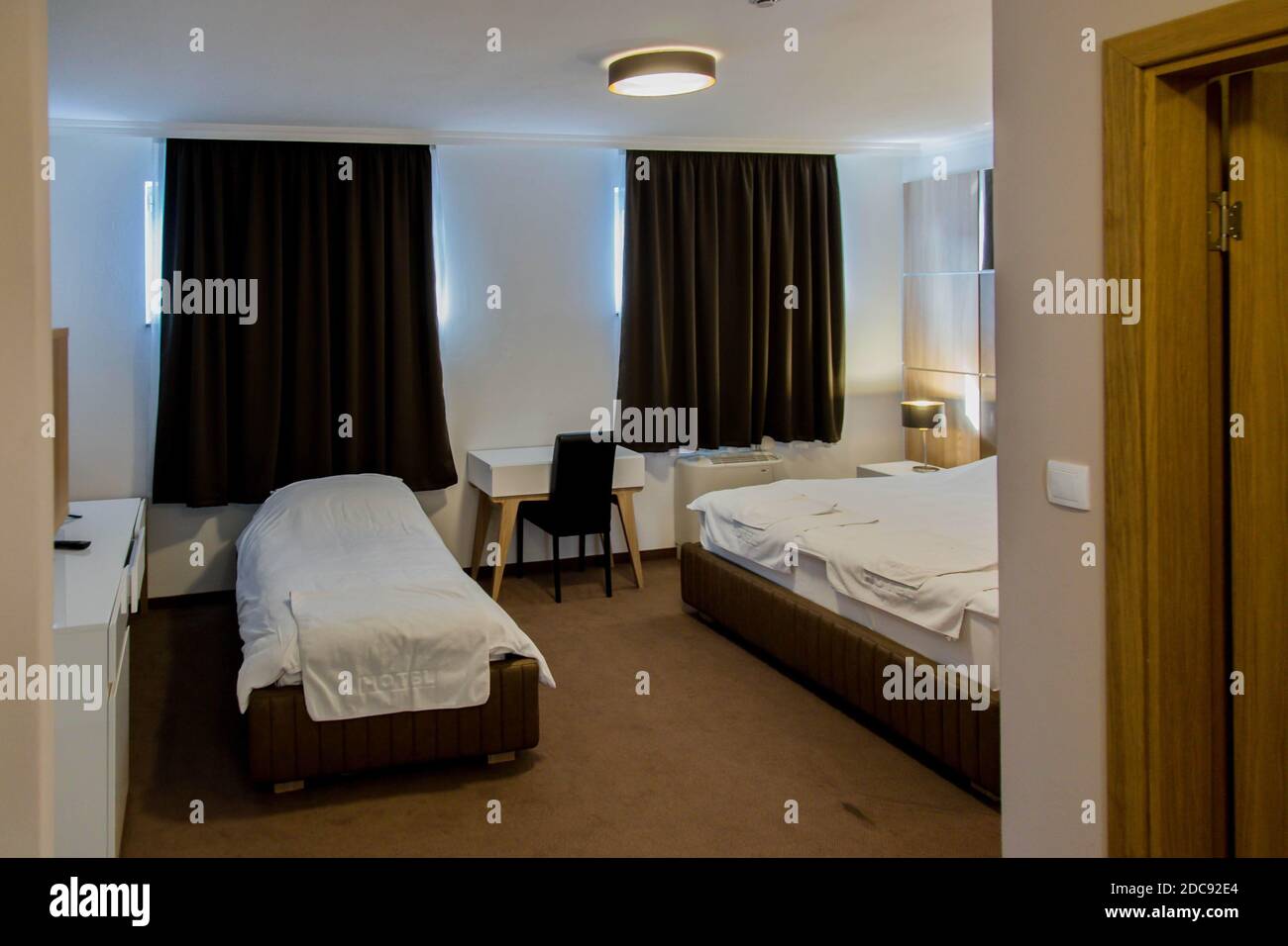 Une chambre triple sous les lumières avec une petite table et rideaux dans un hôtel Banque D'Images