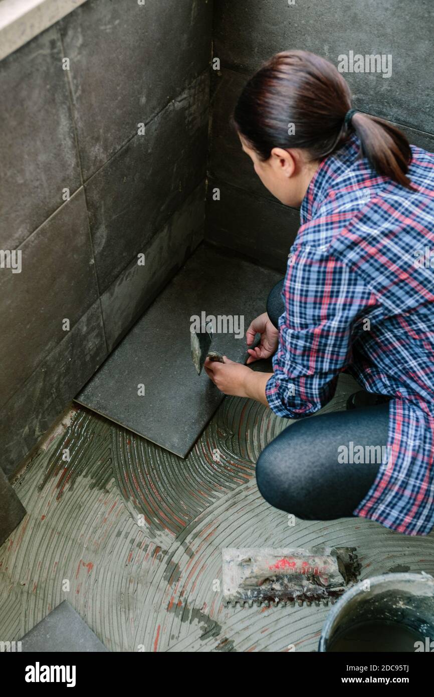 Femme ouvrier posant un nouveau plancher de carrelage Banque D'Images