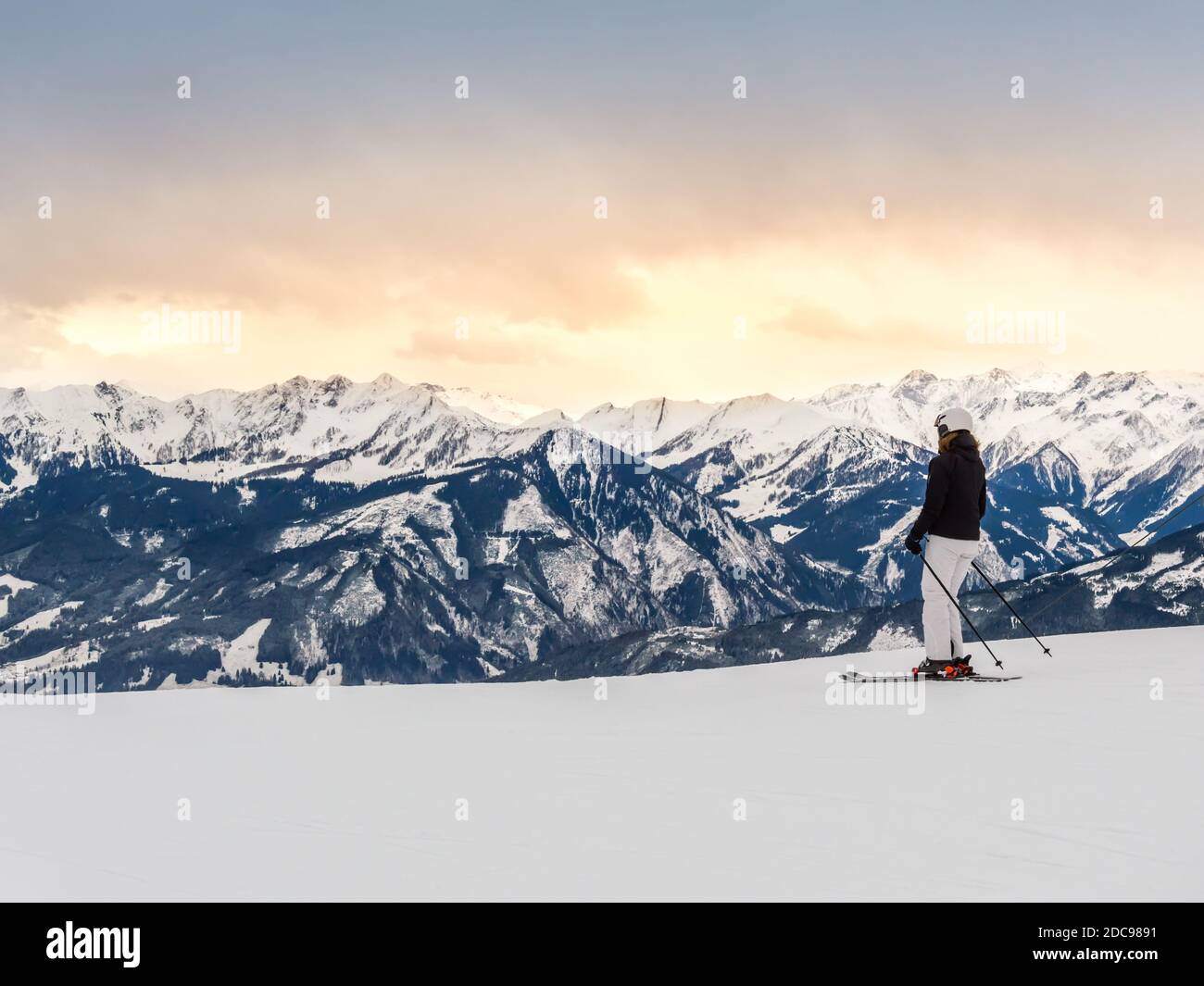 Skieur femelle sur la pente contre les montagnes et coucher de soleil dans la station de ski d'hiver Zell am See dans les Alpes, Autriche. Chaîne de montagnes de Kitzsteinhorn Banque D'Images