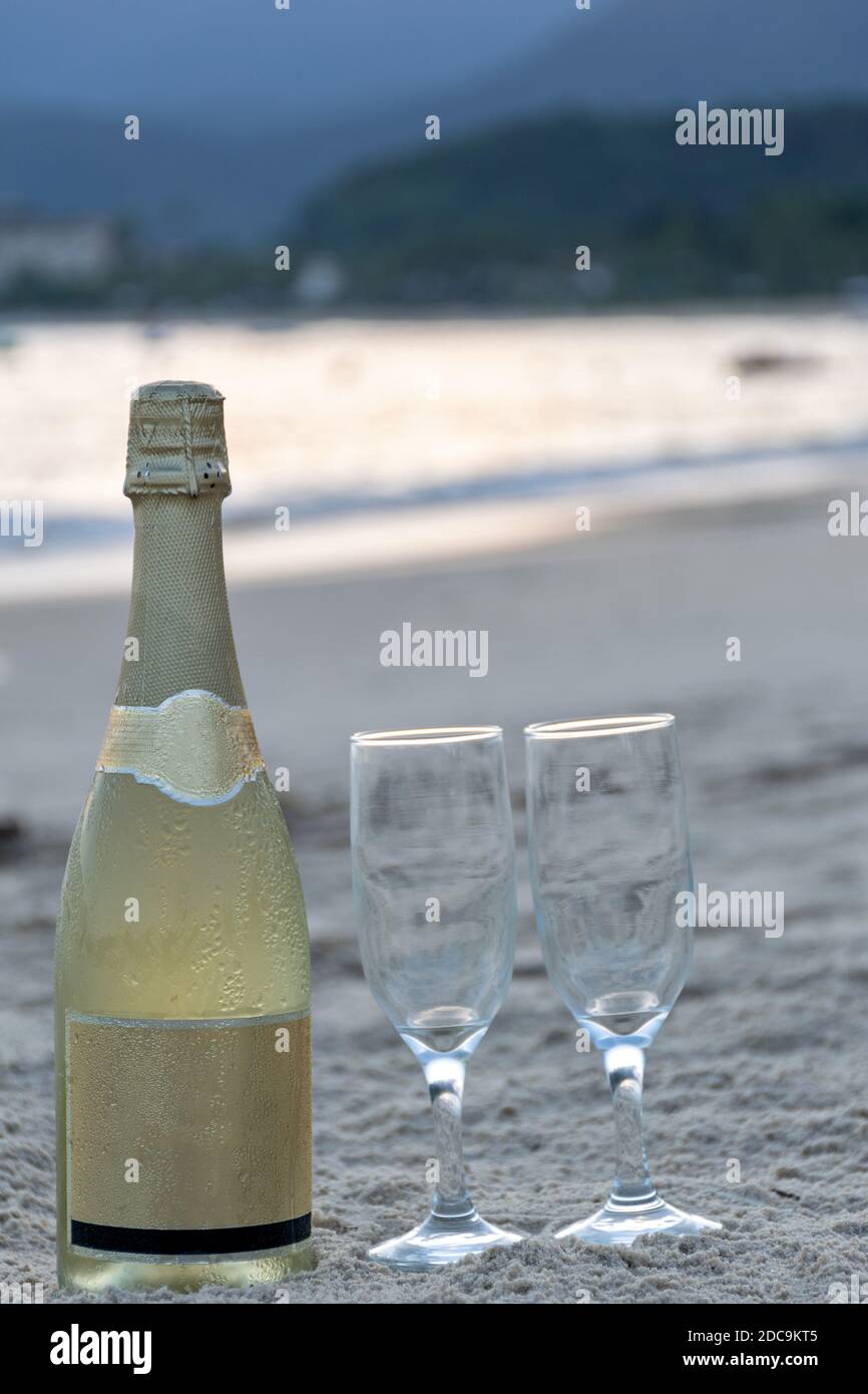 Gros plan d'une bouteille de champagne et de deux verres sur le sable de la plage (photo verticale). Banque D'Images