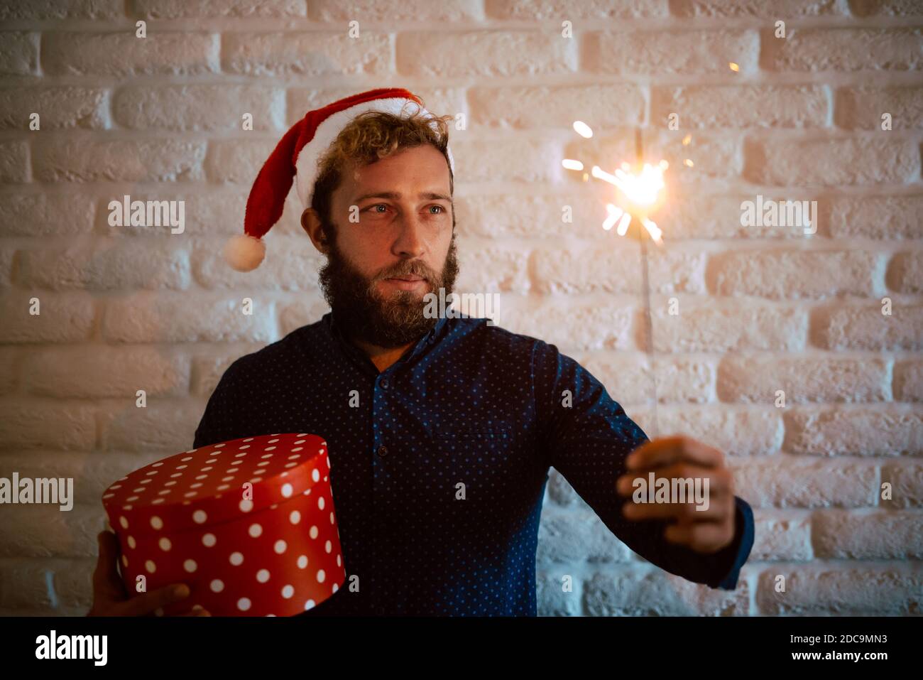 Portrait d'un jeune homme avec un chapeau de Père Noël tenant un flambeau et une boîte cadeau rouge pour la veille de Noël. La magie du nouvel an et de Noël Banque D'Images