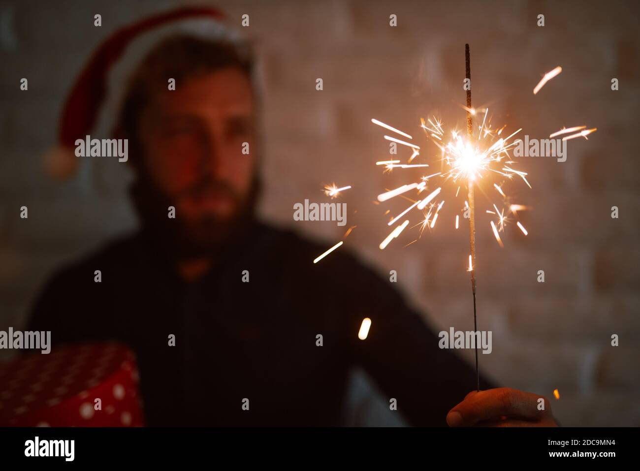 Gros plan d'un arroseur en feu dans la main d'un homme caucasien avec un chapeau de Père Noël pour la veille de Noël. La magie du nouvel an et de Noël Banque D'Images