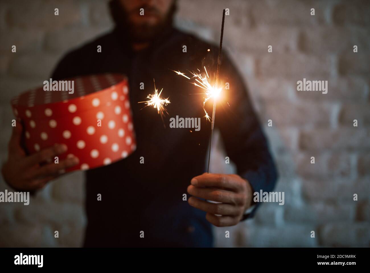 Gros plan d'une arroseur du nouvel an dans les mains d'un jeune homme habillé décontracté tenant une boîte cadeau rouge. Joyeuses fêtes Banque D'Images