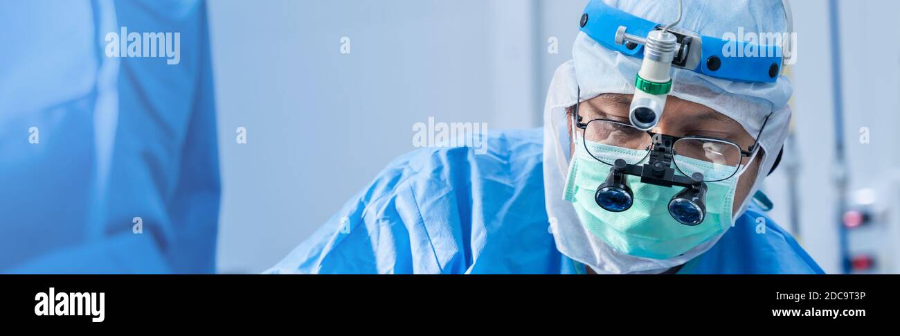 Asiatique médecin chirurgien dans le masque portant des loupes chirurgicales pendant l'intervention médicale, chirurgie salle d'opération avec l'équipement d'électrocauterie pour cardio-vasculaire Banque D'Images