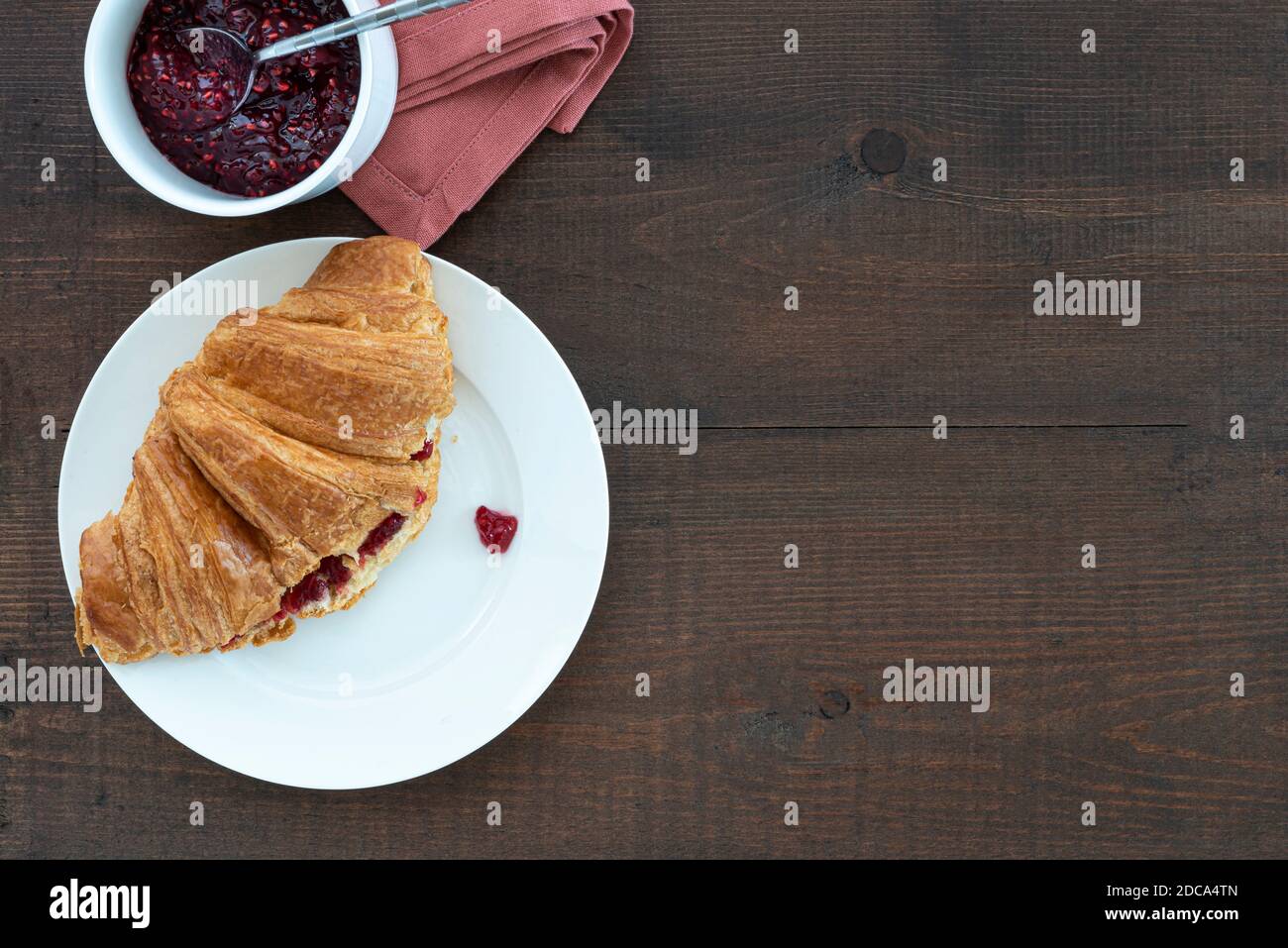 Croissant rempli de confiture sur une assiette, avec une casserole de conservation. Placé sur une table en bois. Banque D'Images