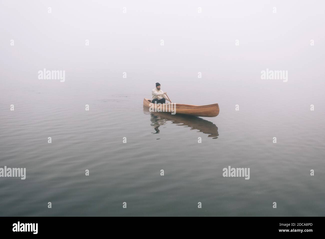 Hipster homme pagaying canoë sur le lac brumeux Banque D'Images