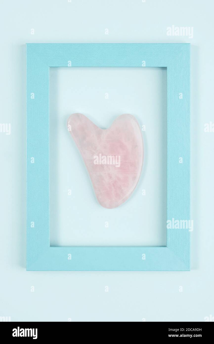Outil de massage jade Gua sha de quartz rose cristal dans le cadre sur fond bleu. Massage facial anti-âge pour un lever naturel et un soin tonifiant au ho Banque D'Images