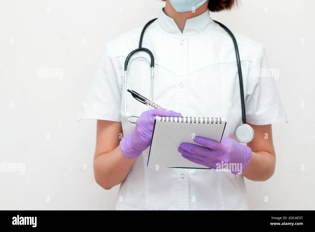 Jeune femme infirmière avec stéthoscope en manteau blanc, gants et masque médical à noter. Banque D'Images