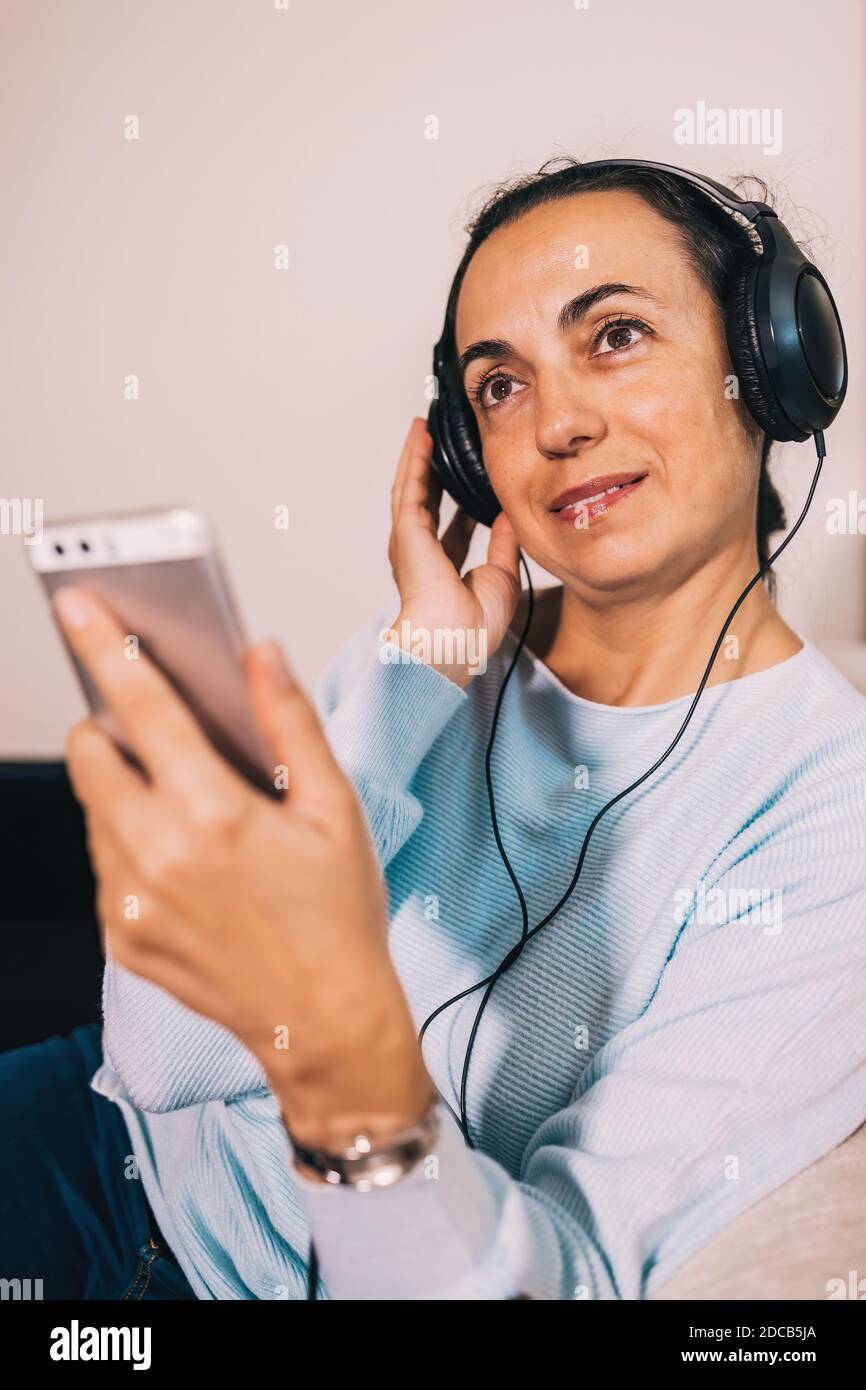Jeune femme espagnole écoutant de la musique à la maison en mobile téléphone avec casque Banque D'Images
