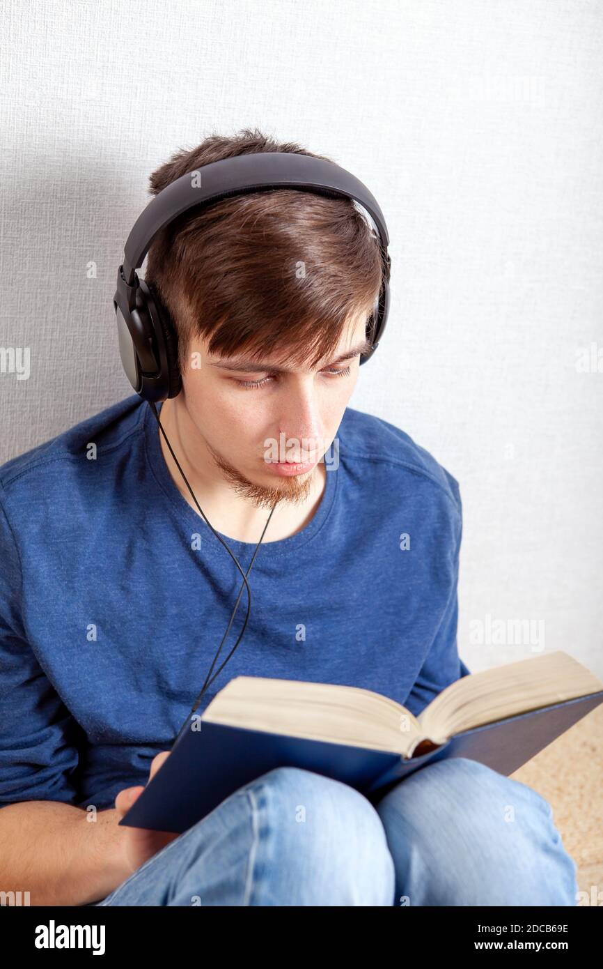 Un jeune homme dans un casque lit un livre à la maison Banque D'Images