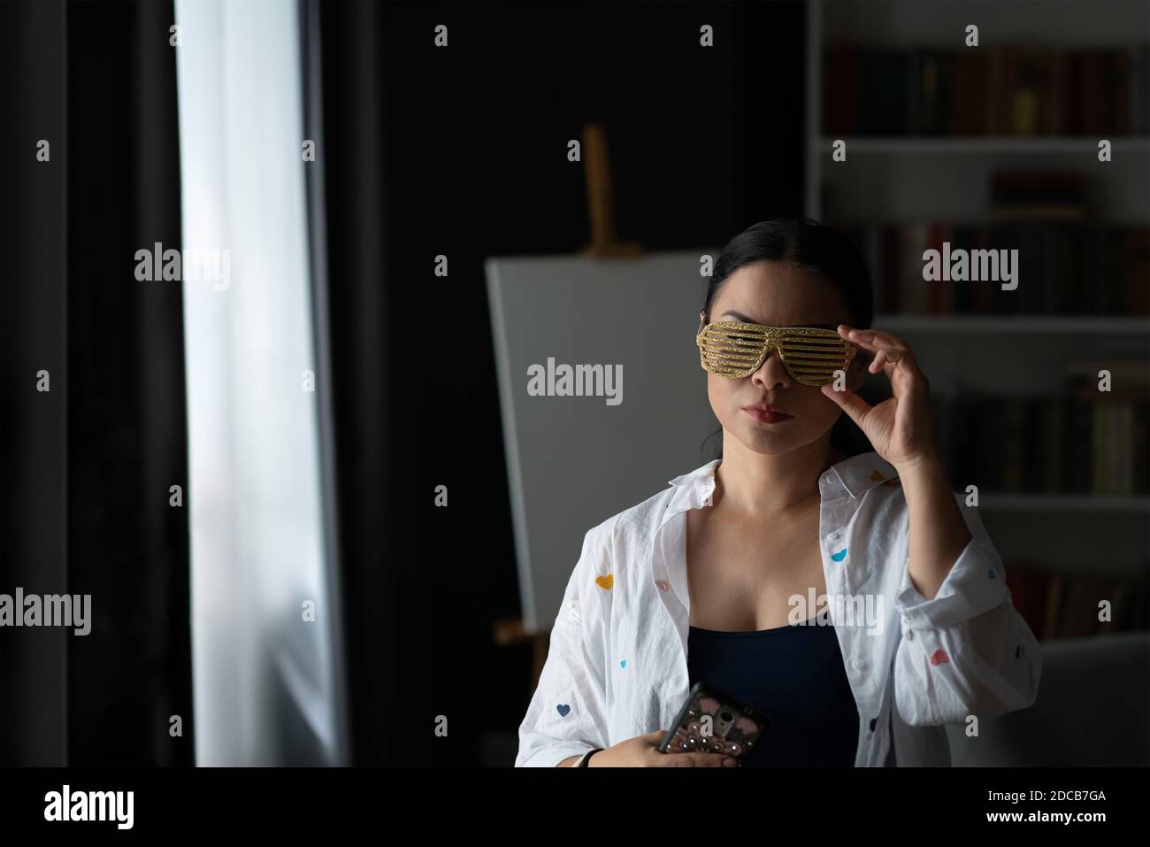 Femme asiatique d'âge moyen est disco des ombres ou des lunettes de fête avec un chevalet derrière elle. Mature sérieux regard à la caméra femme, concept de sensation de bonheur Banque D'Images