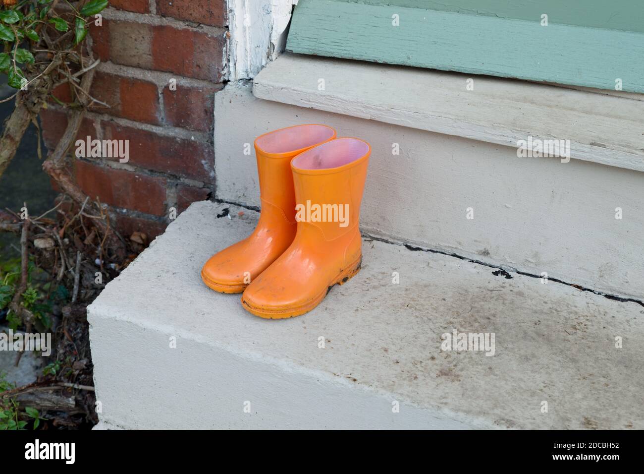 gros plan de la paire de bottes wellington orange vif pour enfants sur un marchepied boueux devant la porte de la maison Banque D'Images