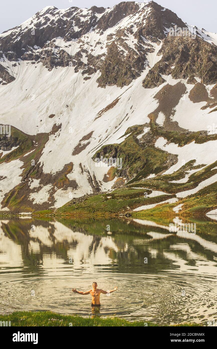 Les jeunes hommes sont des bains touristiques d'un lac de montagne pur et apprécient la nature sur fond de montagnes enneigées. Concept de rétablissement de la santé, wanderlust Banque D'Images
