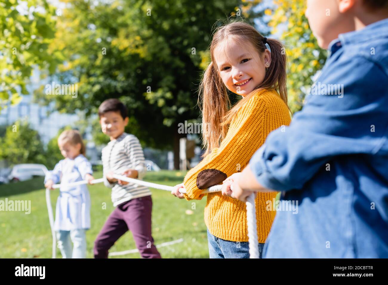 Fille souriante regardant l'appareil photo pendant le tug de jeu de guerre avec des amis sur fond flou dans le parc Banque D'Images