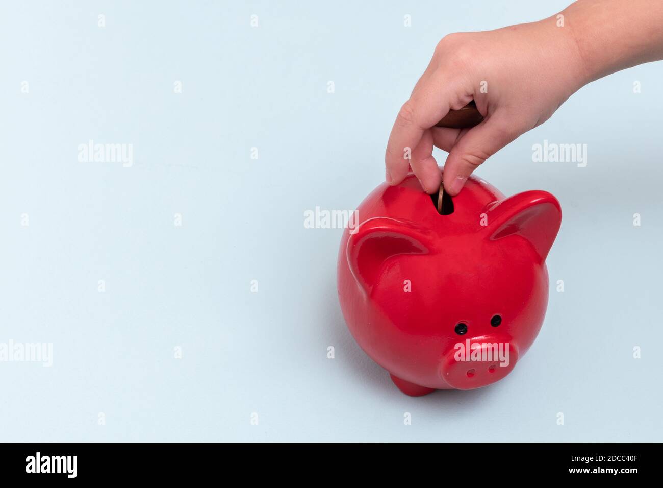 Gros plan de la main d'un enfant met une pièce dans une banque de porc rouge sur un fond bleu, vue du dessus, espace de copie. Concept d'économie d'argent Banque D'Images