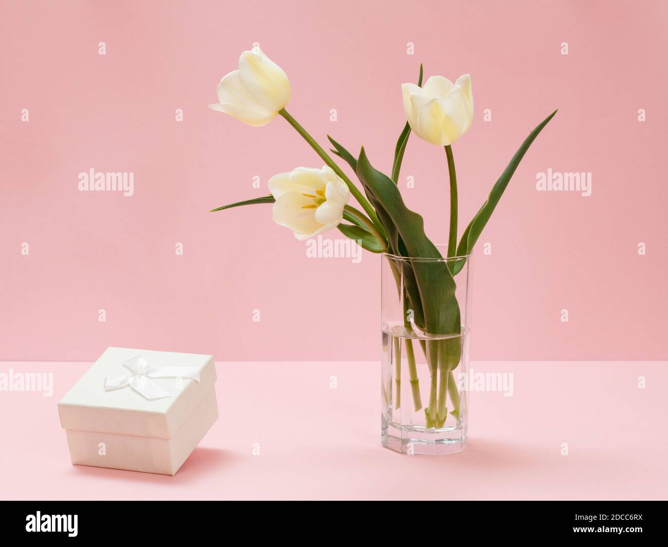 Bouquet de tulipes jaunes dans un vase en verre et boîte cadeau sur fond rose. Banque D'Images