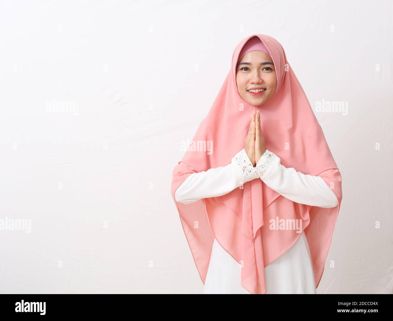 Une femme asiatique en robe musulmane se dresse dans une posture accueillante aux mains de Namaste, accueillant des invités, salutation EEI Fitr. Isolé sur fond blanc Banque D'Images