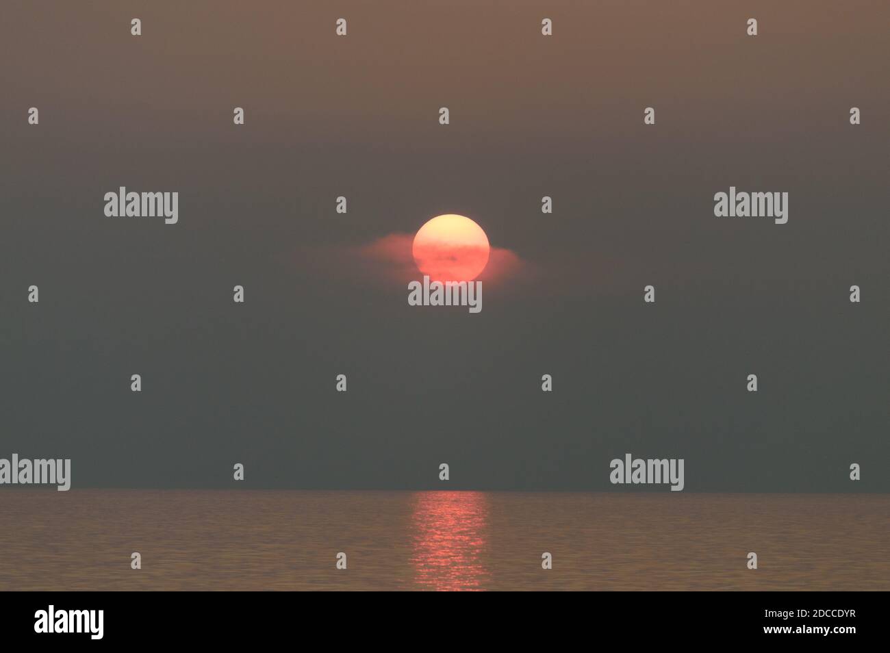 Coucher de soleil sur l'océan, un voile de nuages mince le soleil orange Banque D'Images