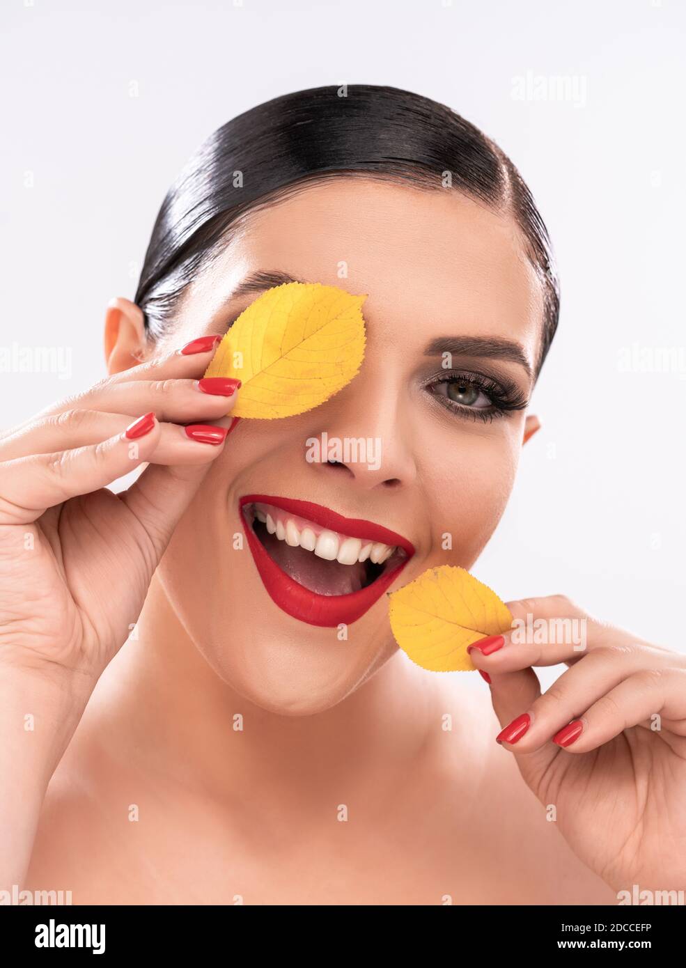 Une femme caucasienne souriante et pieuse tient des feuilles jaunes près du visage comme des taches. Concept de beauté. Isolé sur fond blanc. Gros plan Banque D'Images