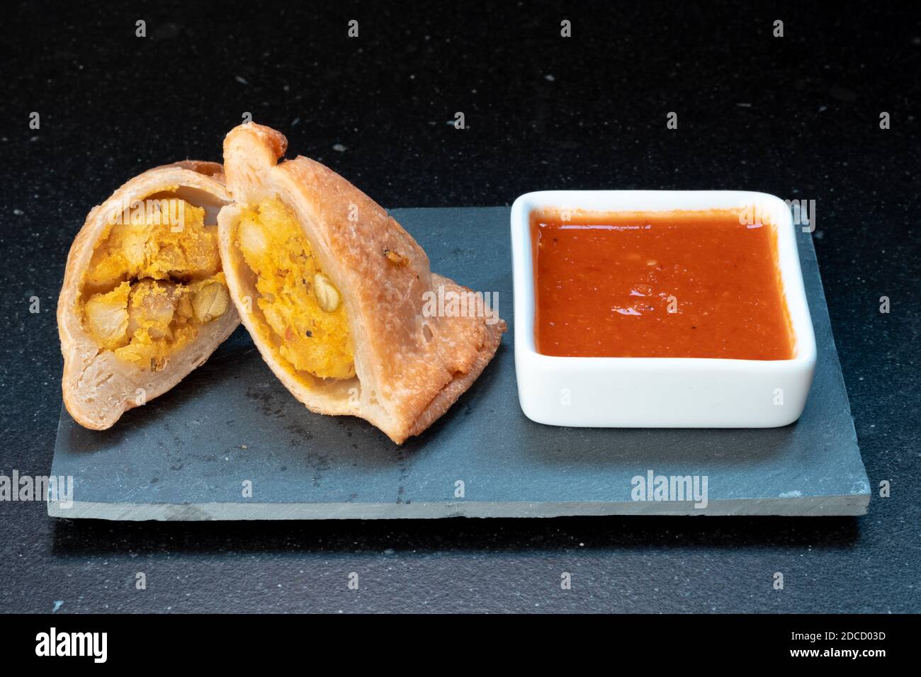 Samosa moderne servi avec une sauce chaude rouge sur un gris et un fond en marbre foncé Banque D'Images