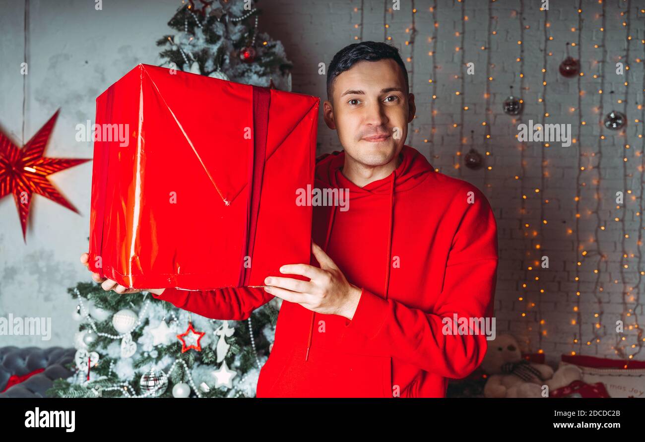 Jeune homme beau avec grand cadeau emballé sur fond d'arbre de Noël. Joli  gars tient une boîte de présent. Concept de vacances, de cadeaux et de  bonne humeur Photo Stock - Alamy
