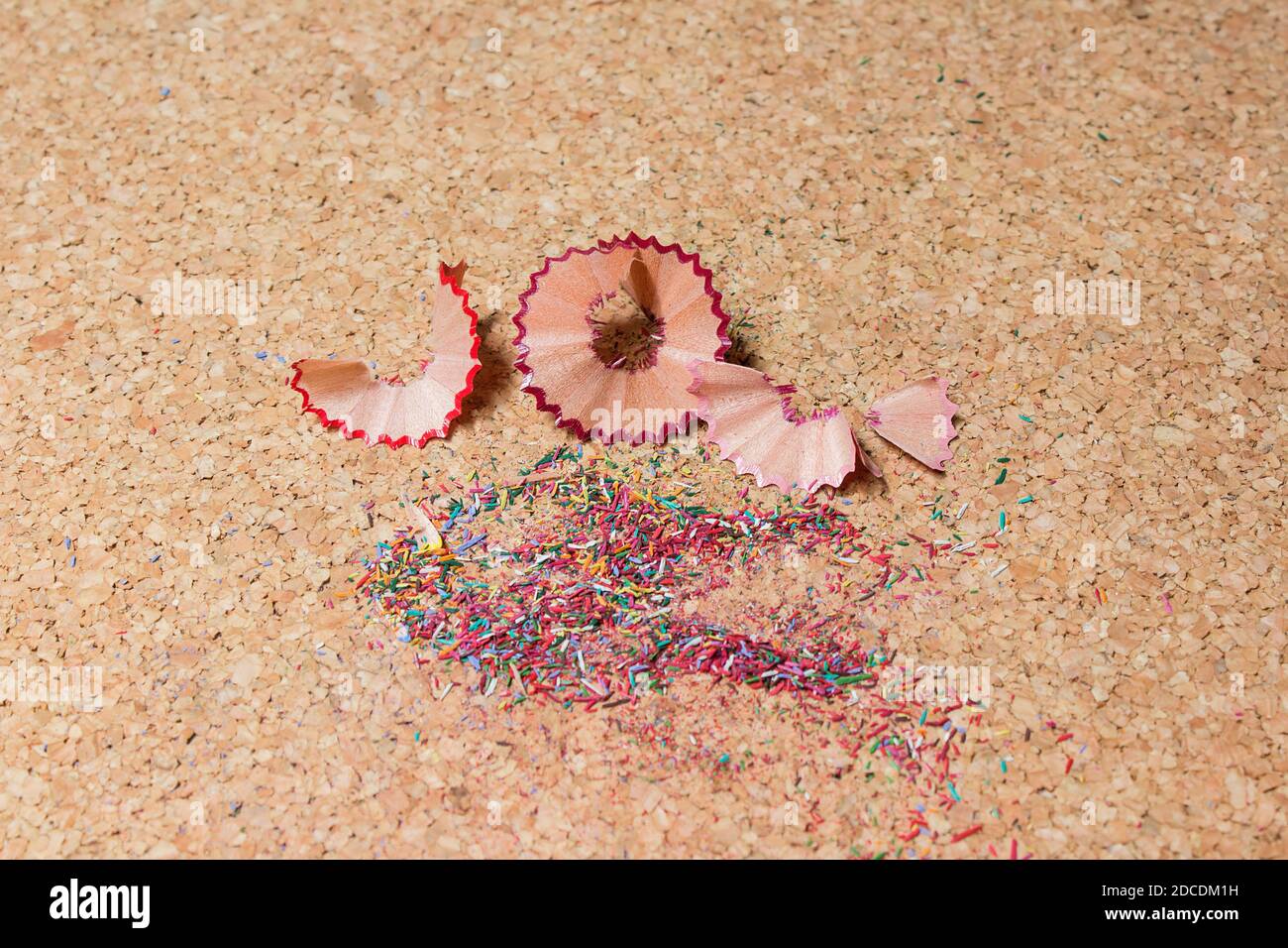 Copeaux de crayons de couleur et morceaux de bois fins de formes géométriques sur un panneau d'affichage en liège. Banque D'Images