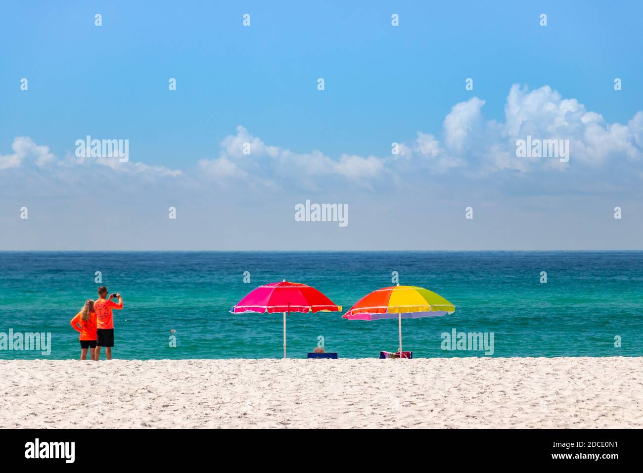 jeune couple en chemises orange dayglo regarder la mer À la plage de Biloxi Mississippi USA avec des tons de soleil colorés parasols Banque D'Images