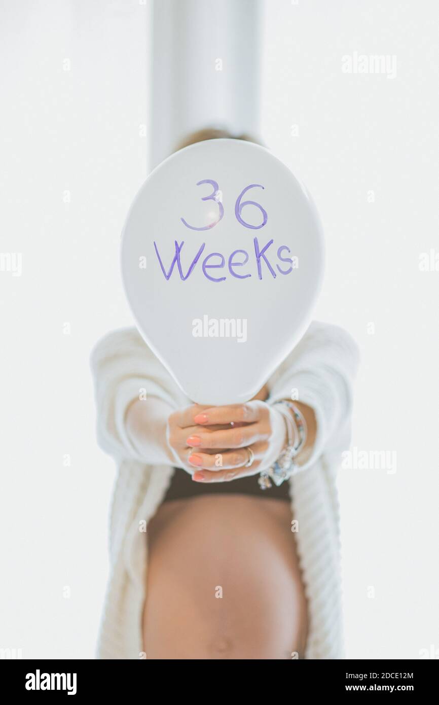 Une femme enceinte tient un ballon avec les mots '36 semaines' - la jeune fille enceinte est derrière et prend dans la main le ballon pendant la maternité ti Banque D'Images
