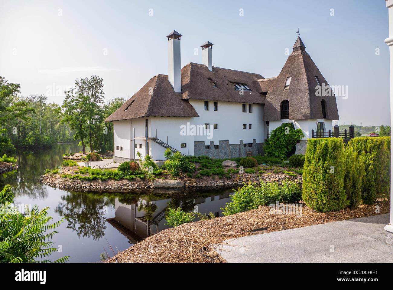 Photo d'une maison de trois étages avec un toit en roseaux, cheminées et dormeurs sur les rives du lit de la rivière. Ciel bleu. Photo horizontale Banque D'Images