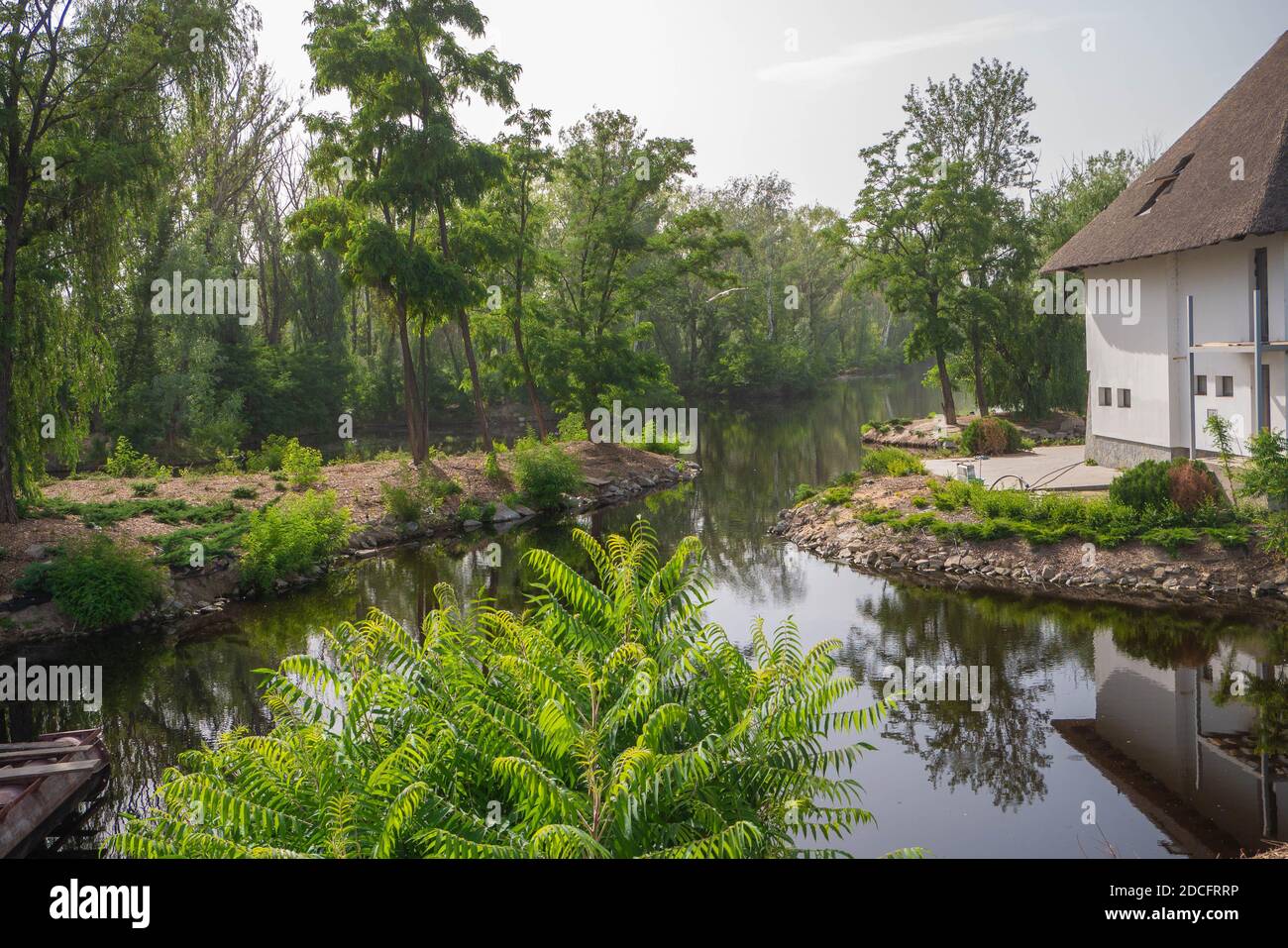 Une photo horizontale d'une rivière qui passe devant une maison aux murs blancs et une rive aux grands arbres verts. Jour. Ciel dégagé. Paysage Banque D'Images