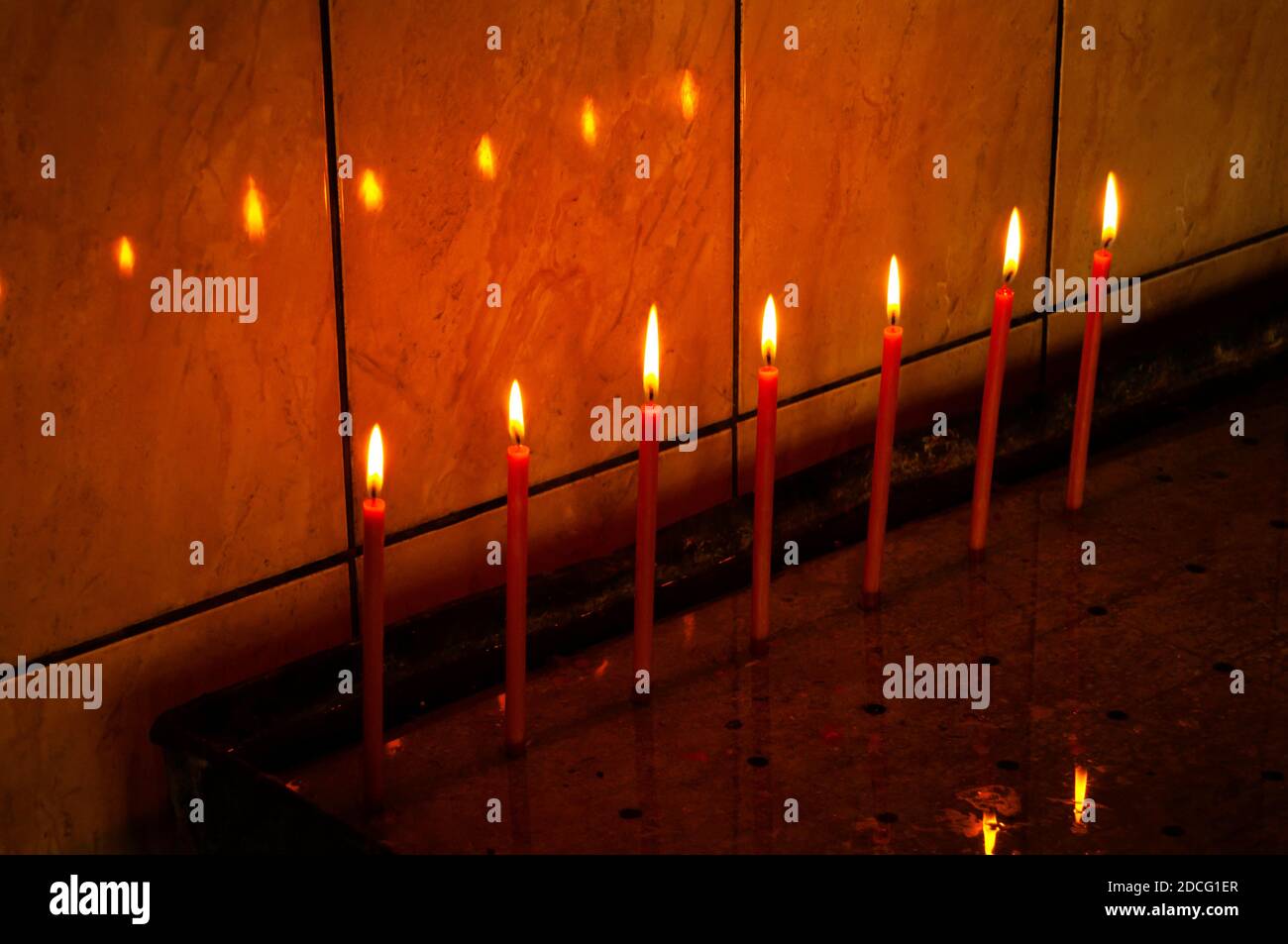 Sept bougies colorées en soirée à l'église. Lumière dans l'obscurité, réflexion sur le mur. Banque D'Images