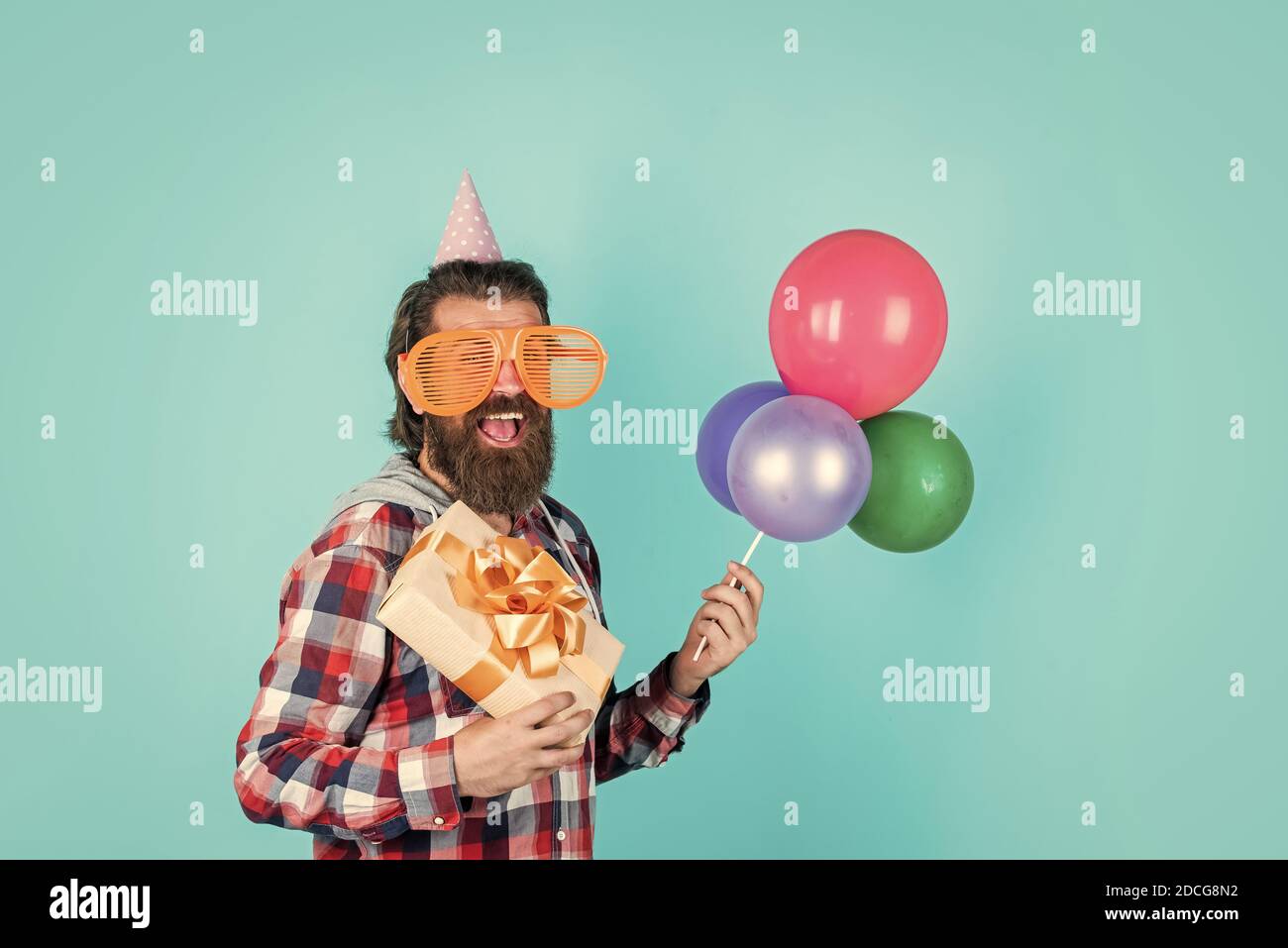 Quoi acheter. Gestionnaire d'événements avec boîte cadeau. Homme brutal en fête. Homme drôle en chapeau d'anniversaire. Joyeux Noël. Fête de la fête, fou. S'amuser avec des ballons. Préparez-vous pour un anniversaire. Banque D'Images