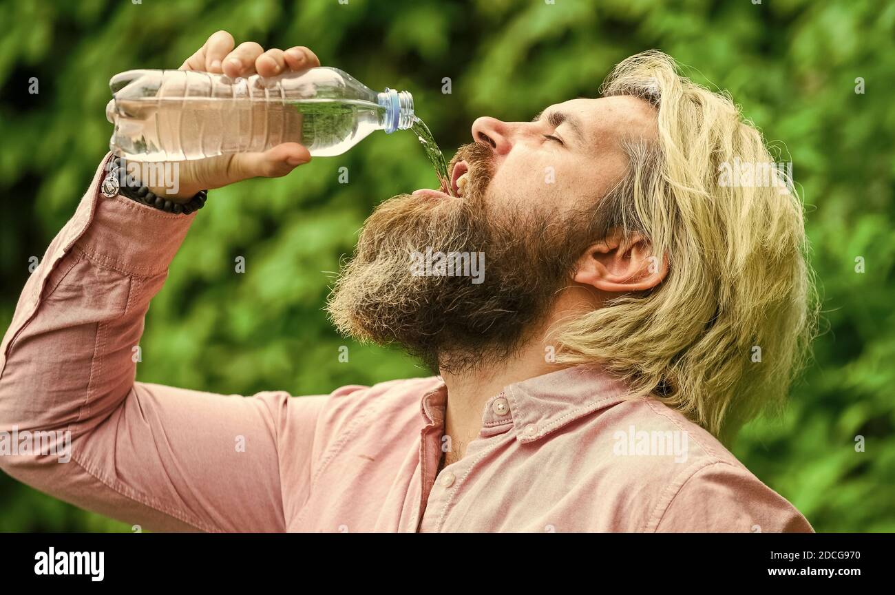 Équilibre de l'eau. Homme barbu touriste eau potable bouteille plastique nature fond. Un gars assoiffé qui boit de l'eau en bouteille Un mode de vie sain. Sécurité et santé. Chaleur estivale. Boire de l'eau claire. Banque D'Images