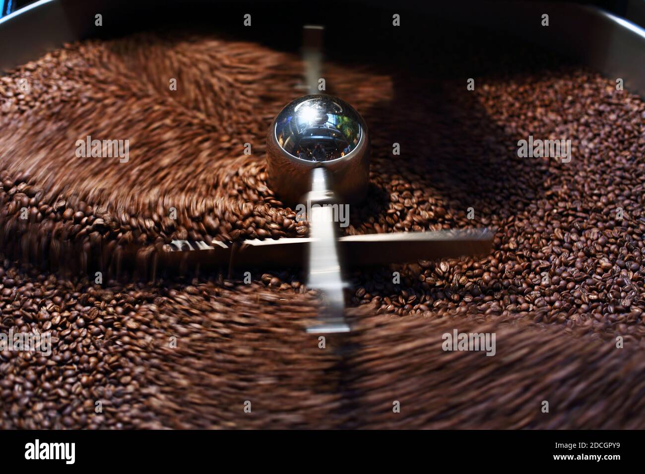 Les grains de café fraîchement torréfié provenant d'un grand torréfacteur de café est versé dans le cylindre de refroidissement. Motion Blur sur les haricots. Banque D'Images