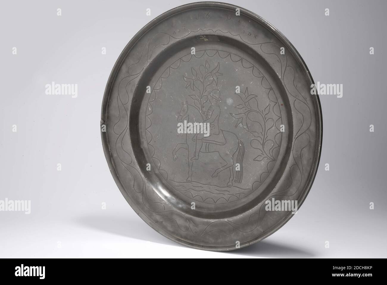 Soucoupe, Anonyme, 1801, moulé, général: 2.7 x 37,6cm 27 x 376mm, soucoupe de Pewter gravée avec l'image d'un cavalier avec une branche de fleur dans sa main. L'année 1801 est gravée avec les lettres ADN en bas à gauche et les lettres BDN en bas à droite. Un motif ornemental ondulé peut être vu tout autour du bord. Une ancienne réparation est visible dans le bord de la soucoupe à gauche de l'image, 1919 Banque D'Images