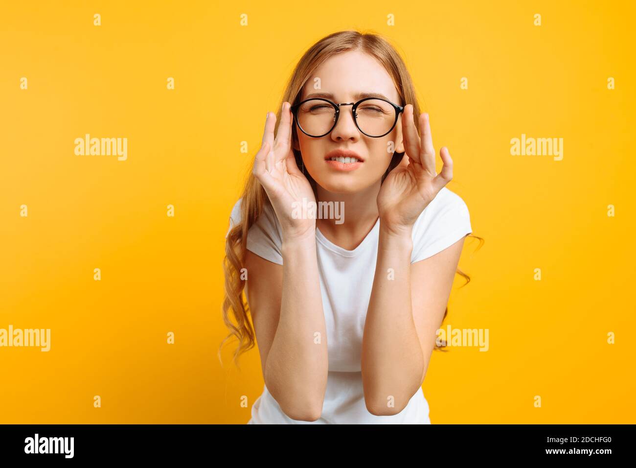 Une fille dans un T-shirt blanc, avec une mauvaise vue porte des lunettes, regardant s'accroupir, essayant de comprendre ce qui est écrit sur un fond jaune Banque D'Images
