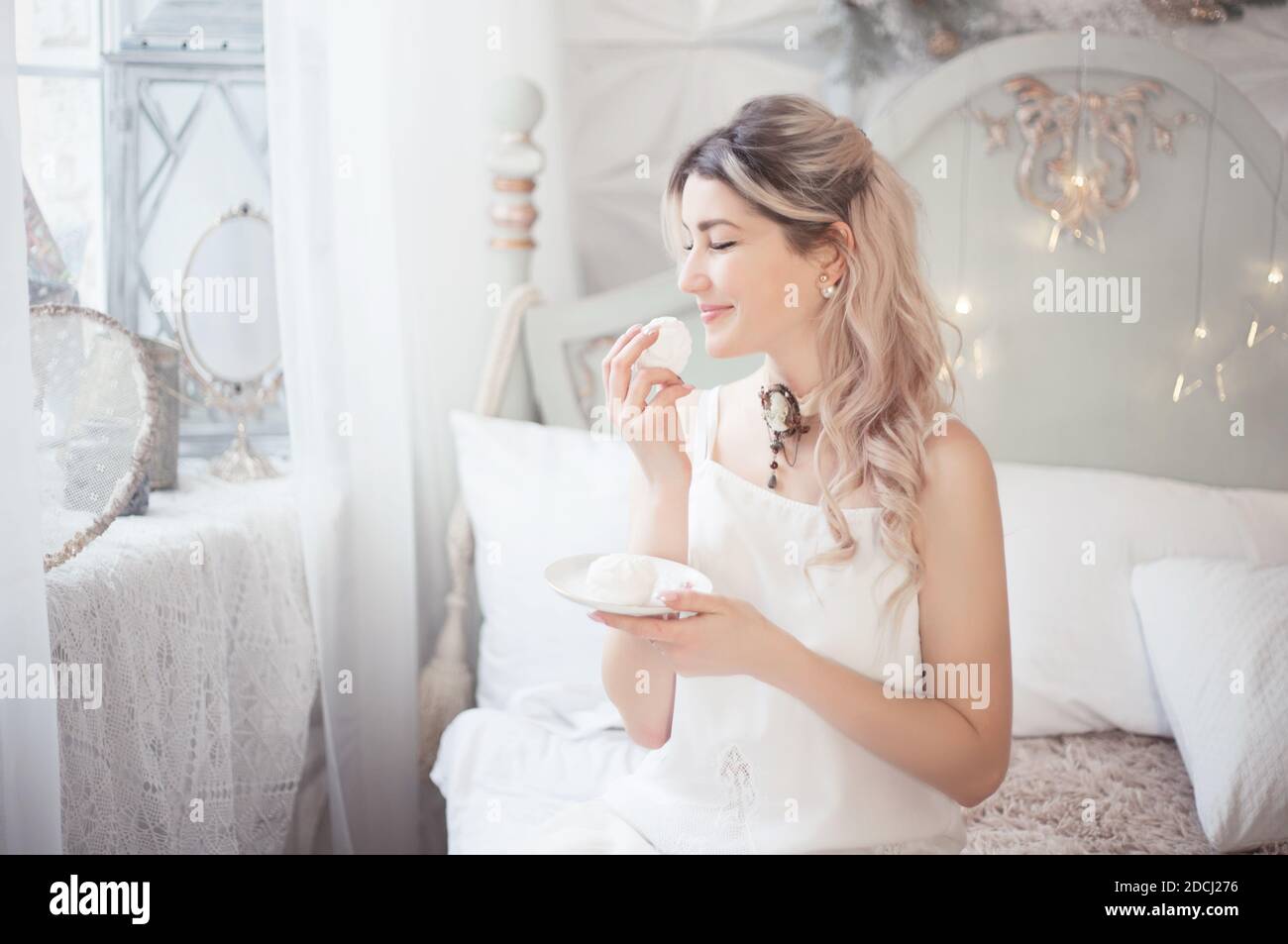 Jolie jeune femme mangeant des bonbons le matin dans la chambre. Doux matin d'hiver. Photo de studio. Banque D'Images