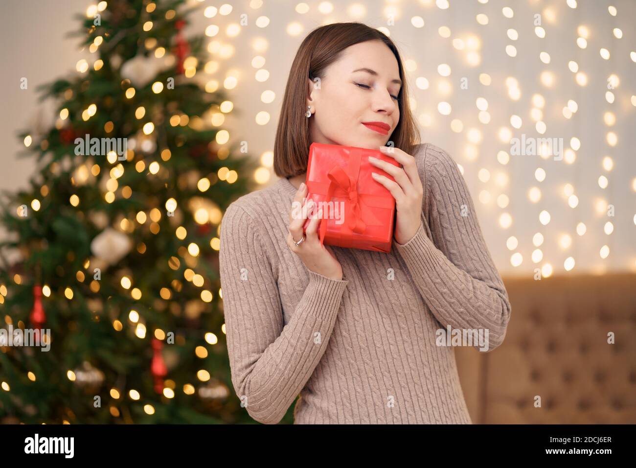 Portrait de jeune femme heureuse lèvres rouges posant avec une boîte cadeau emballée. Gros plan la femme satisfaite a reçu la boîte actuelle. Rétro-éclairage de Noël festif Banque D'Images