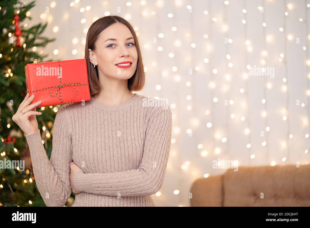 Portrait de jeune femme heureuse lèvres rouges regardant l'appareil photo tenant une boîte cadeau emballée. Gros plan la femme satisfaite a reçu la boîte actuelle. Noël festif Banque D'Images