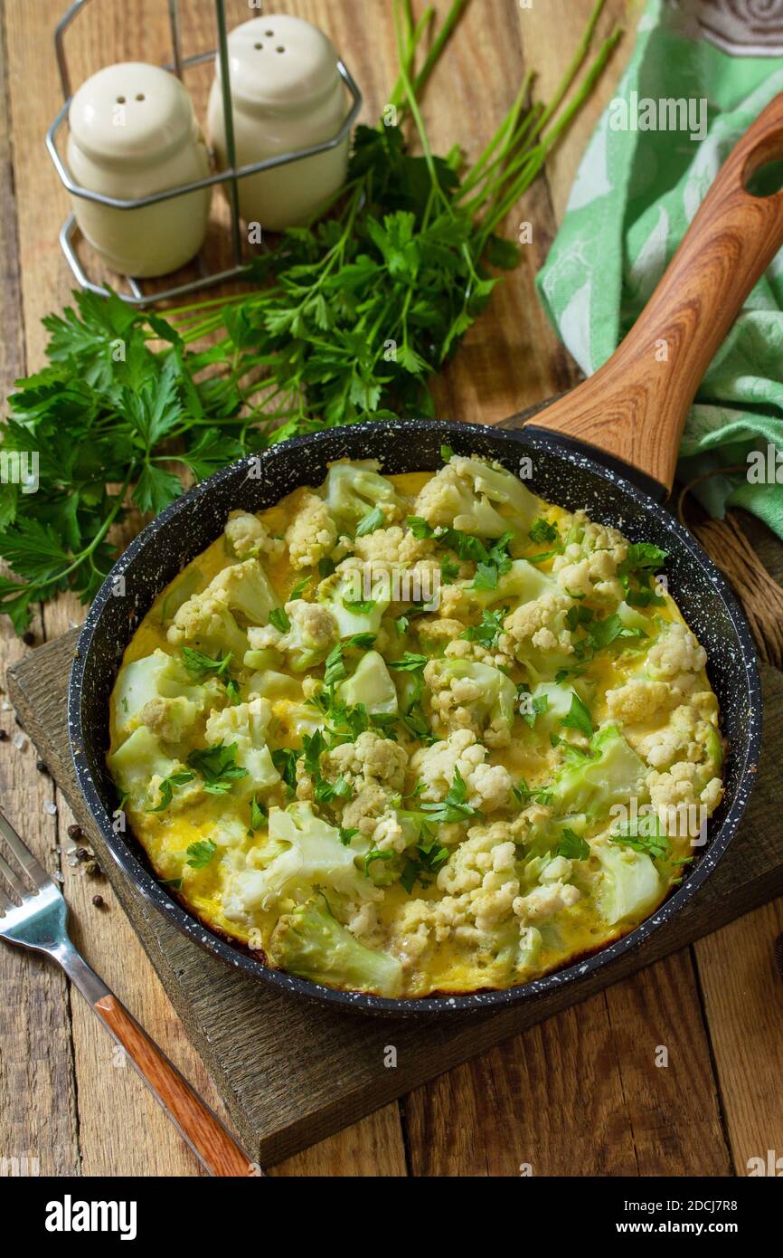 Un petit déjeuner diététique ou un déjeuner sain. Omelette aux oeufs avec chou-fleur dans une poêle en fonte sur une table rustique en bois. Banque D'Images