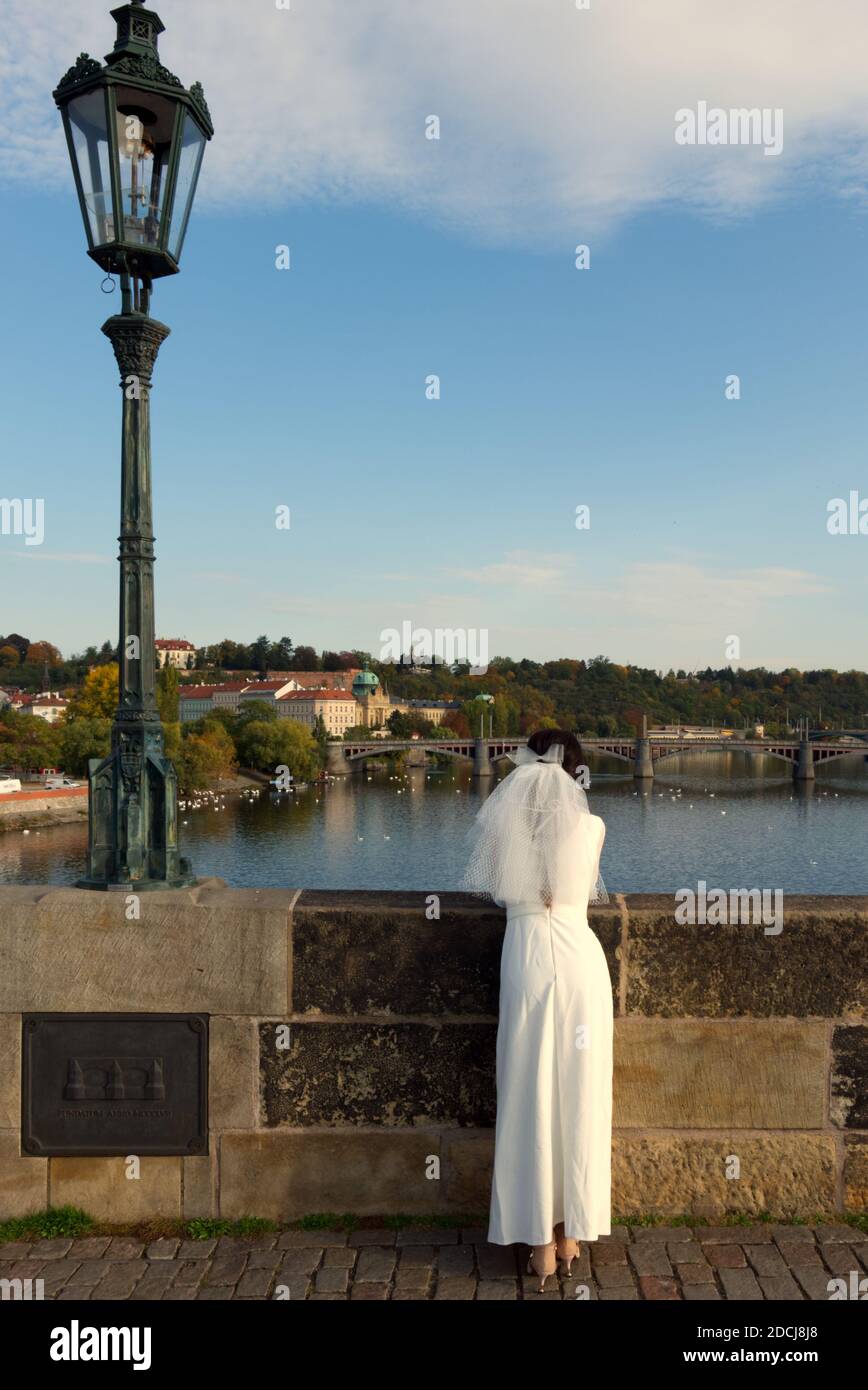 La mariée admire Prague depuis le pont Charles. Fille dans une robe de mariage avec un voile. Banque D'Images